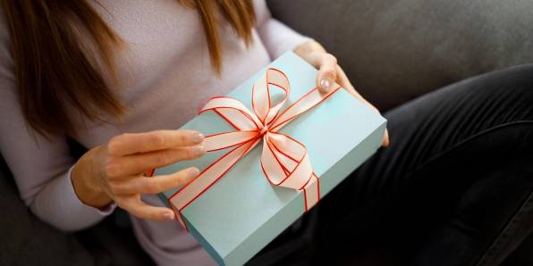 Frau sitzt auf einem Sofa und hält ein blau verpacktes Geschenk in der Hand.